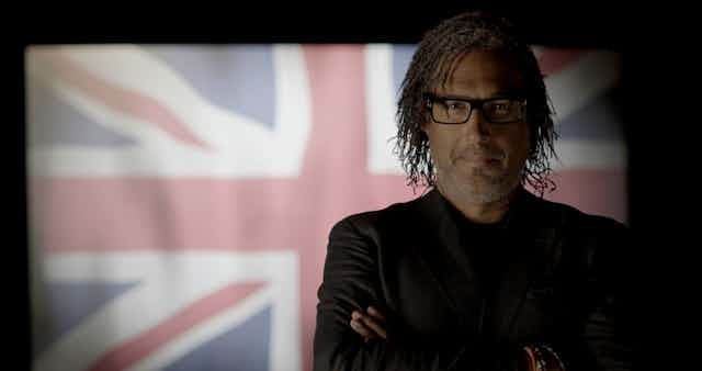 David Olusoga stands with crossed arms in front of a union flag 