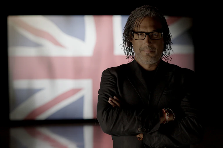 David Olusoga stands with crossed arms in front of a union flag