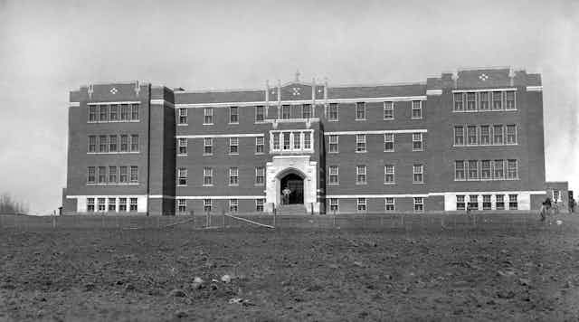 A black and white photo of a large brick building, large lawn in front.  