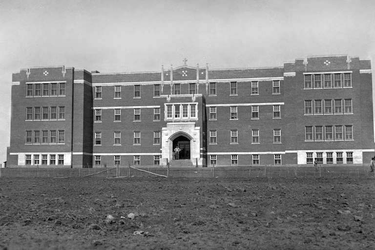 A black and white photo of a large brick building, large lawn in front.
