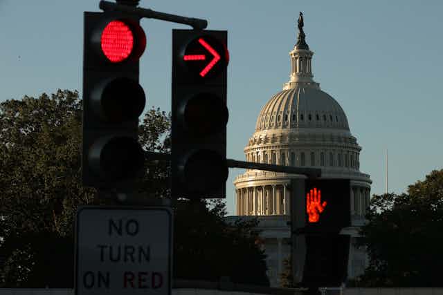 The US Capitol is seen at sunrise, with a red stop light and red crossing sign. 
