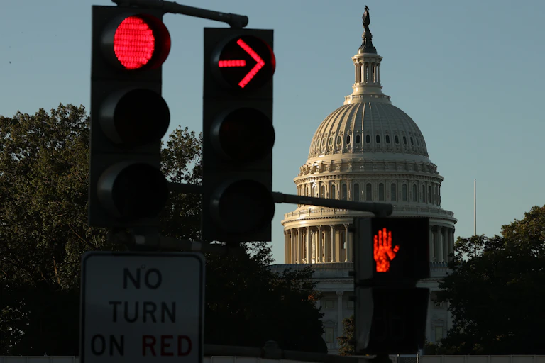 The US Capitol is seen at sunrise, with a red stop light and red crossing sign.