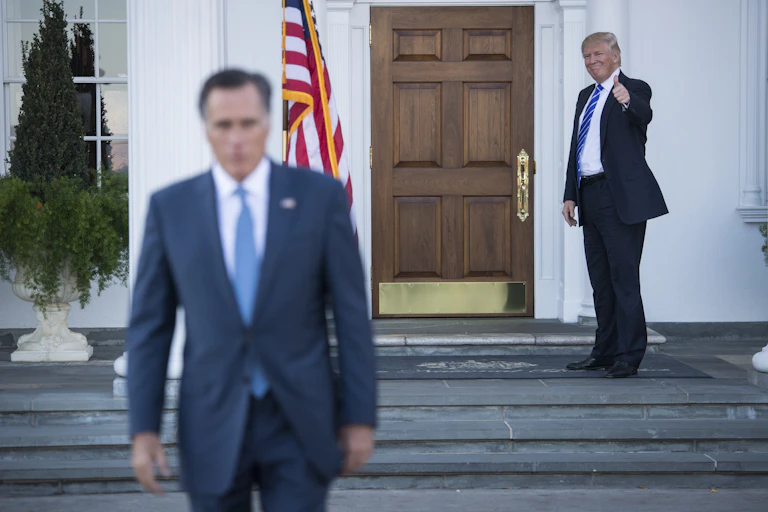 Two men, one in a blue suit and one in a dark suit, with one leaving and the other waving.