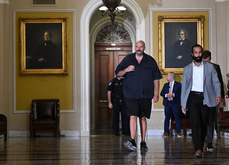 Bald mustached man in shorts, sneakers and sleveless T-shirt.