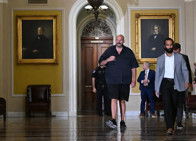 Bald mustached man in shorts, sneakers and sleveless T-shirt.