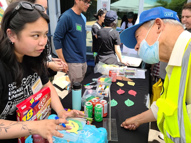A young woman seen speaking with an elderly man in a face mask.