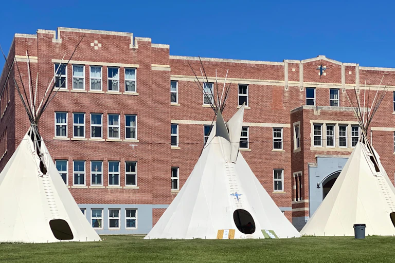 Three white tipis outside a brown stone building