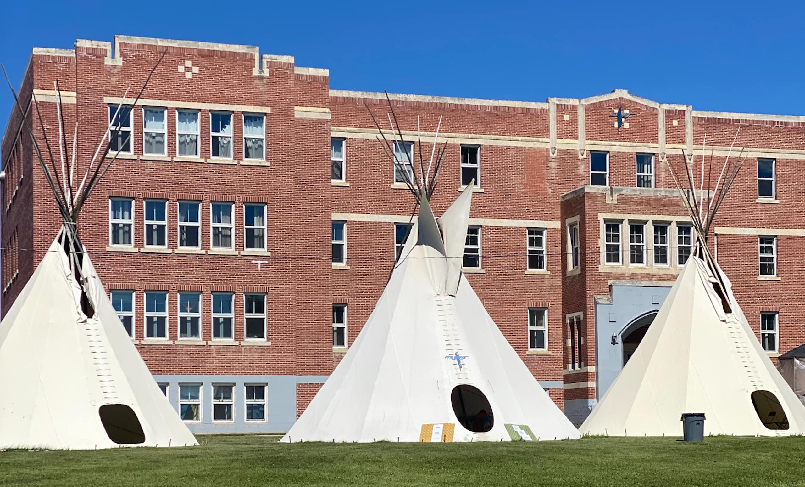 Three white tipis outside a brown stone building