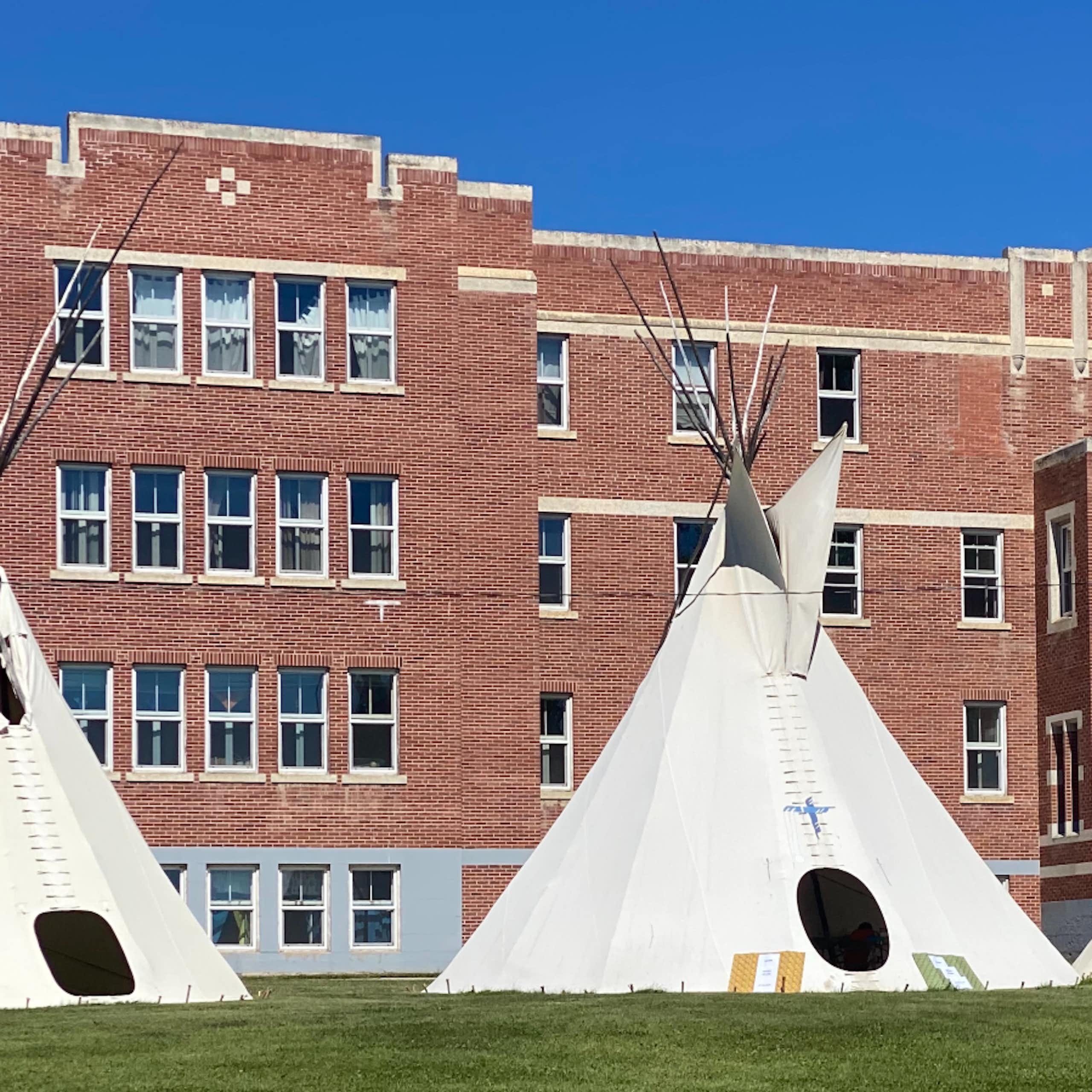 Three white tipis outside a brown stone building