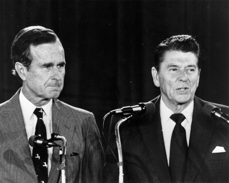 Two men in suits and ties in front of microphones.