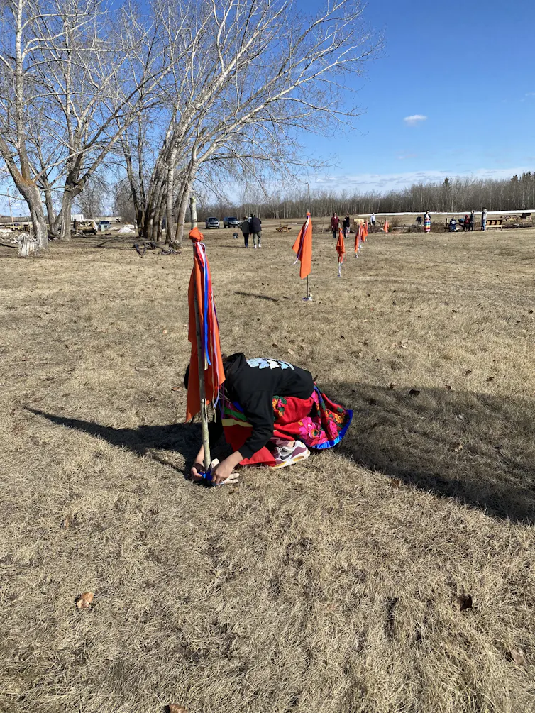 a young person bends down on the grown near a stake marking a spot on the lawn