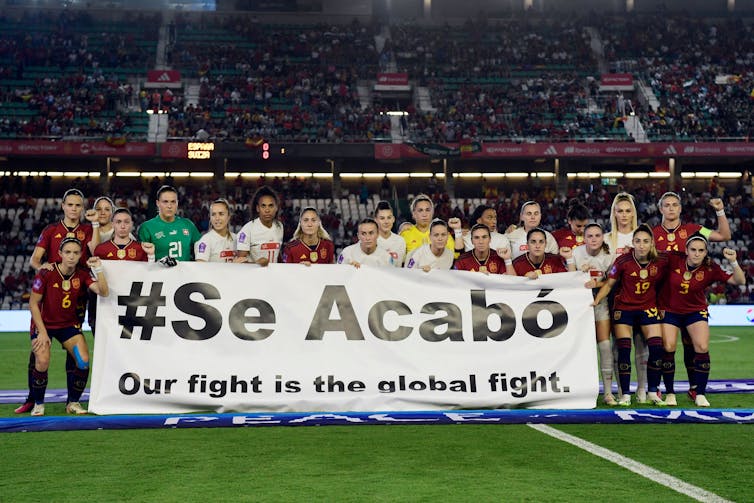 Female soccer players stand over a banner reading 'It's over. Our fight is the global fight.'