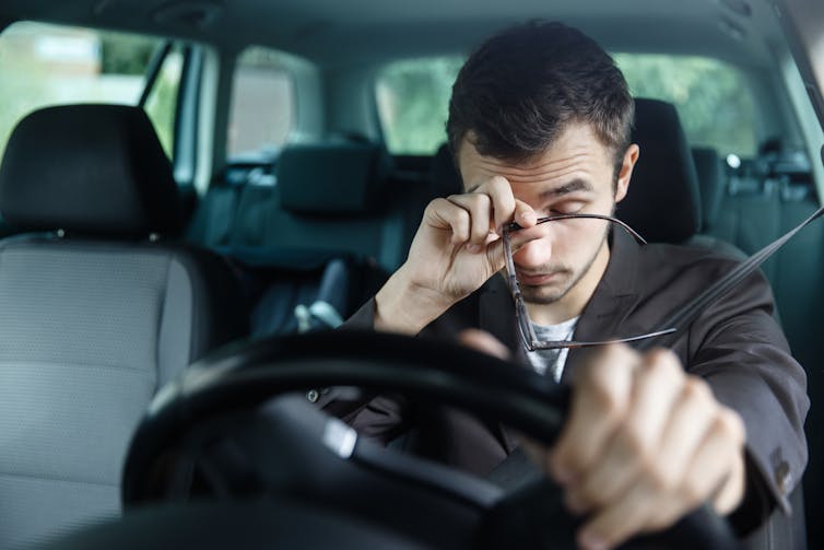A man rubs his eyes while sitting behind the steering wheel of a vehicle
