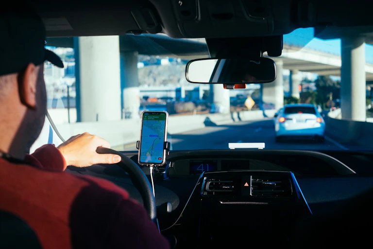 Over-the-shoulder view of a man in a baseball hat driving while using a mounted cellphone to navigate
