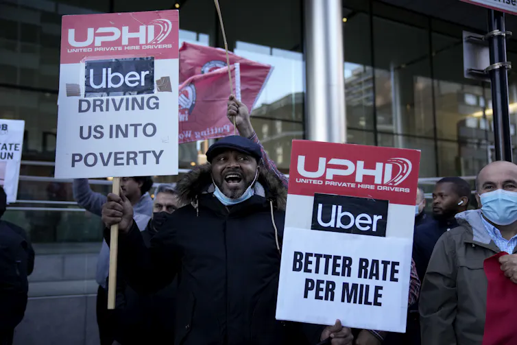 People hold protest signs demanding higher pay from Uber