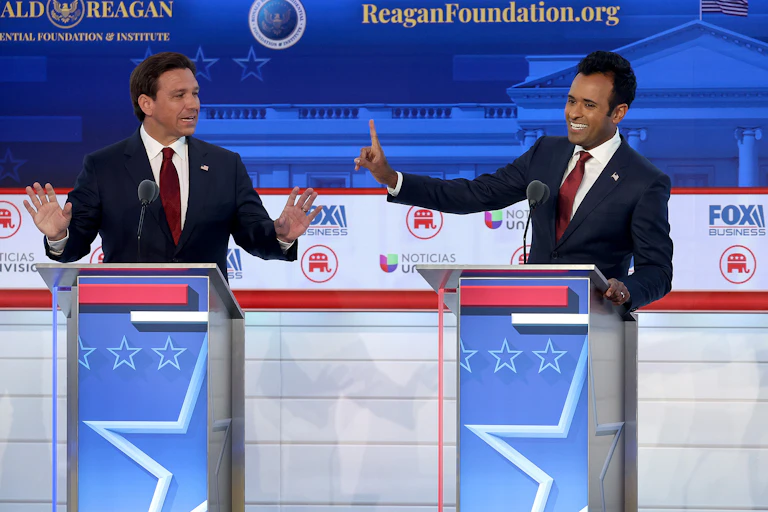 Two men gesticulate at lecterns, one wagging his finger at the other.