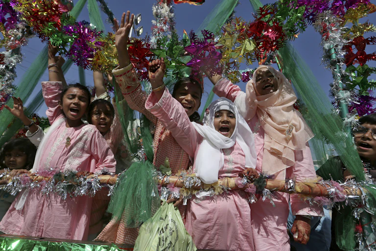 Five girls in pink outfits wave excitedly among colorful streamers.