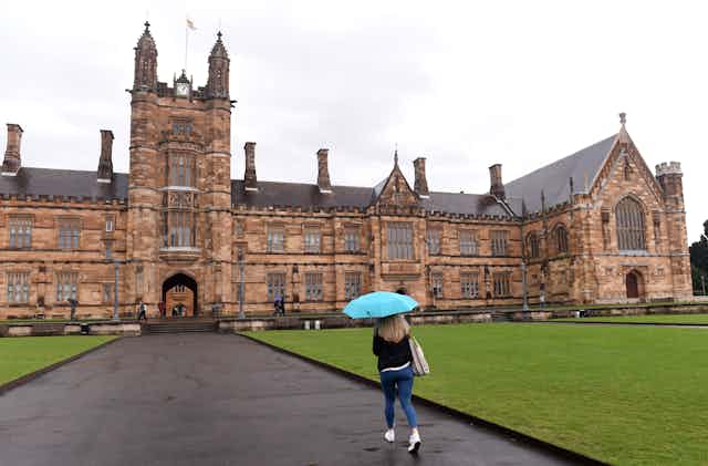 A woman under an umbrella approaches the the main building at Sydney University. 