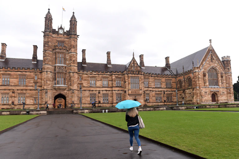 A woman under an umbrella approaches the the main building at Sydney University.