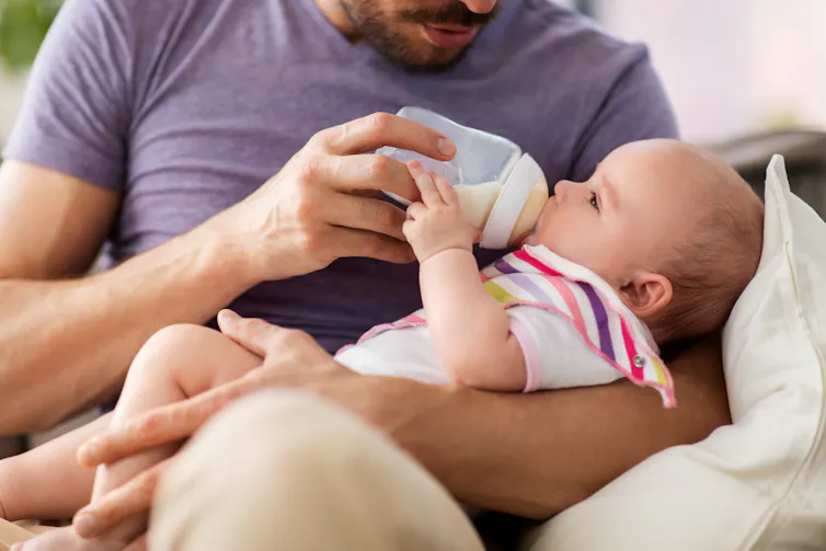 A man feeds a baby with a bottle.