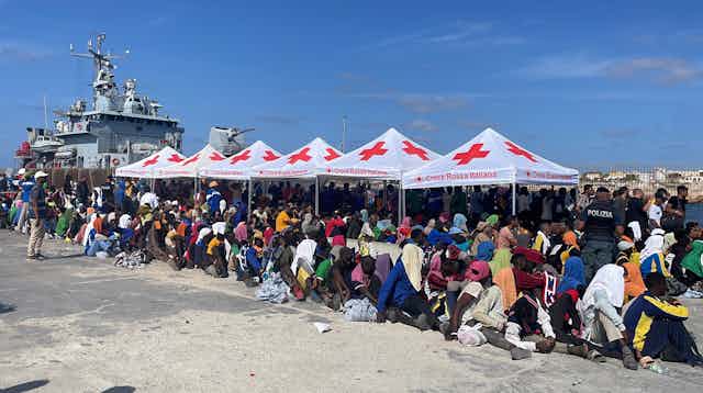 Numerosos migrantes bajo toldos de la Cruz Roja en el puerto de Lampedusa.