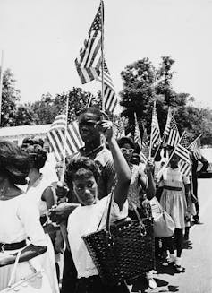 A group of Black teenagers carry American flags as they protest against the murder of a civil rights leader.