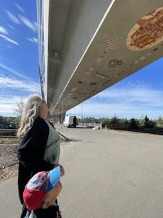 A woman with a boy looking up at a bridge.