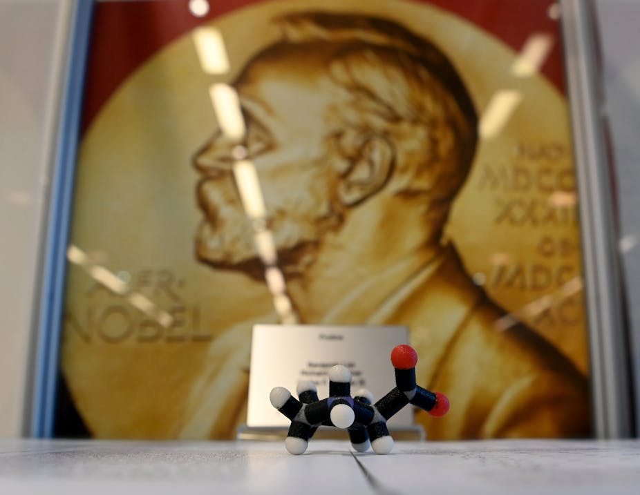 model of a molecule sits in front of a poster of gold Nobel award