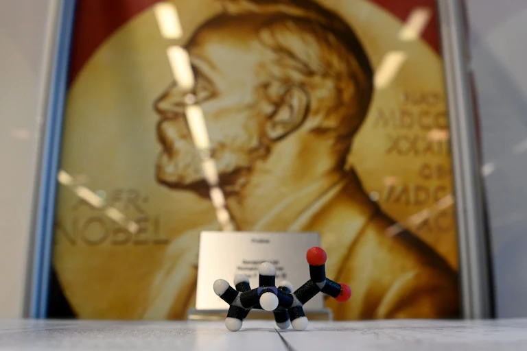 model of a molecule sits in front of a poster of gold Nobel award
