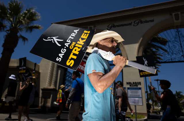 Man wearing cowboy hat and sunglasses holds sign reading 'SAG-AFTRA on strike!'