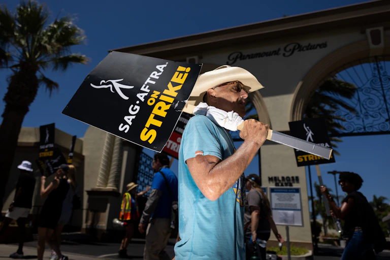 Man wearing cowboy hat and sunglasses holds sign reading 'SAG-AFTRA on strike!'