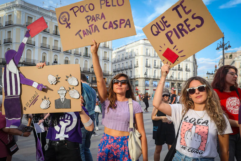 A group of protestors with a cardboard placard depicting a bald man being shown a red card from a referee