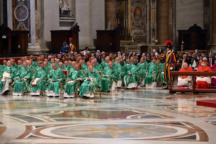 Clergymen in green robes seated in the pews.