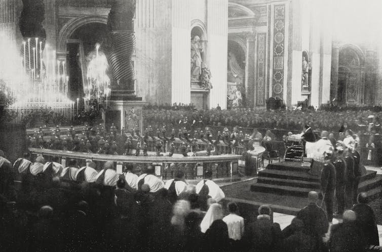 A black and white image showing a large number of people seated in pews.