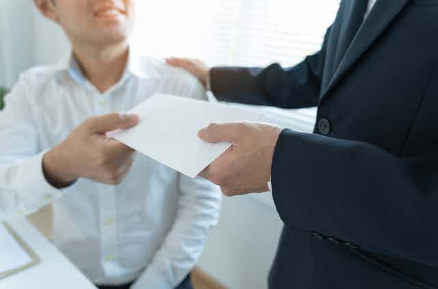 A man in a suit handing another man, who is seated, a blank envelope