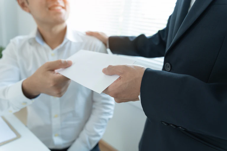A man in a suit handing another man, who is seated, a blank envelope