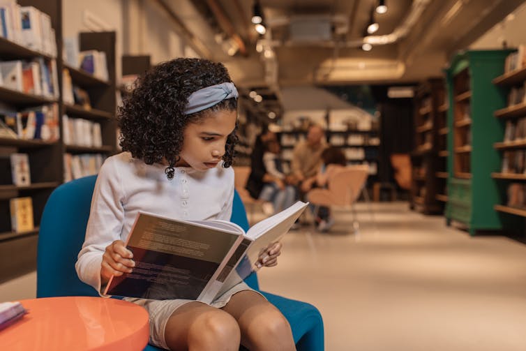 A girl sits in a library reading a book.