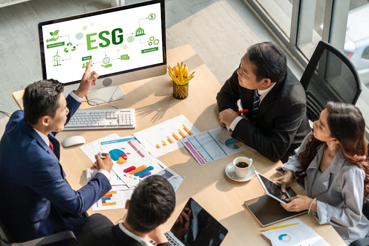 A group of people in business attire sit around a table and look at a computer screen with the letters ESG on it
