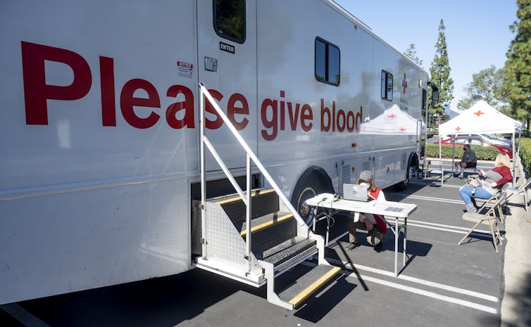 A white trailer with the words 'Please give blood' emblazoned on it in bold red letters.