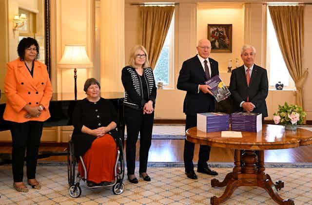 5 people pose for photo with pile of official documents in formal room