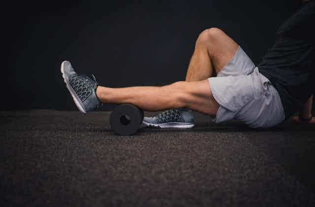 A man uses a foam roller on his leg.
