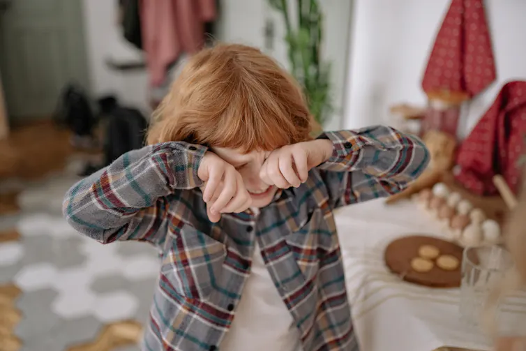 A young child puts their hands on their eyes and cries.
