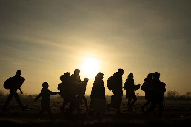 Silhouette of families walking across a field with a yellow sky and low sun behind them