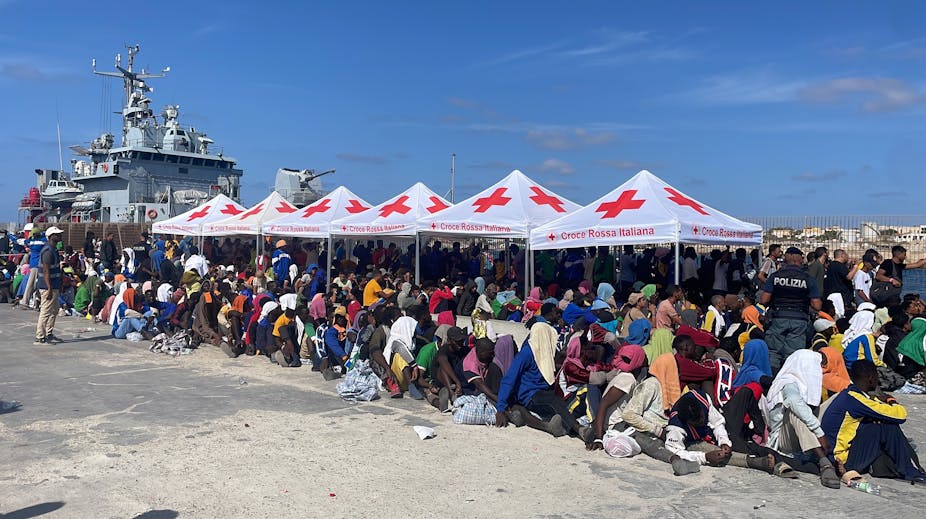 A large number of migrants sitting under Red Cross shelters in the port of Lampedusa.