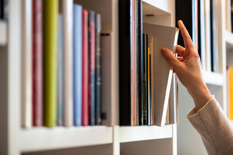Main de femme cherchant un livre sur une étagère