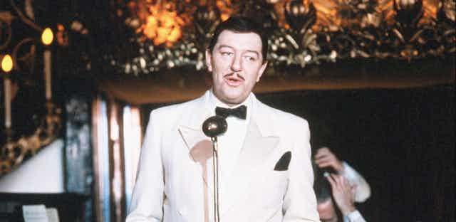 A man dressed in a white tux crooning into a microphone.