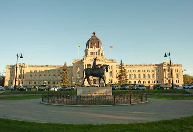 A large white domed building with a stature of a man on a horse in front. 