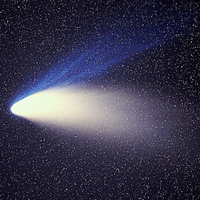 A bright comet streaking downward, with blue and white streaks of light following behind, against a backdrop of black and many small white stars. 