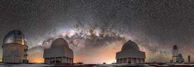 Large telescopes domes at night with Milky Way in background sky.