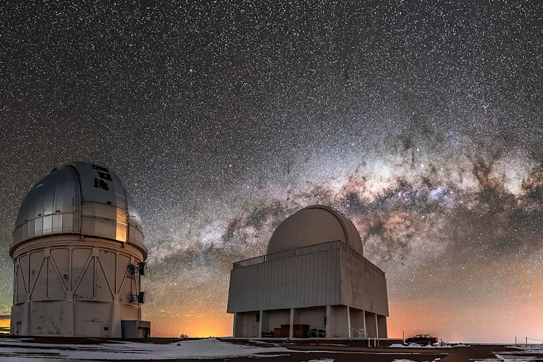 Large telescopes domes at night with Milky Way in background sky.